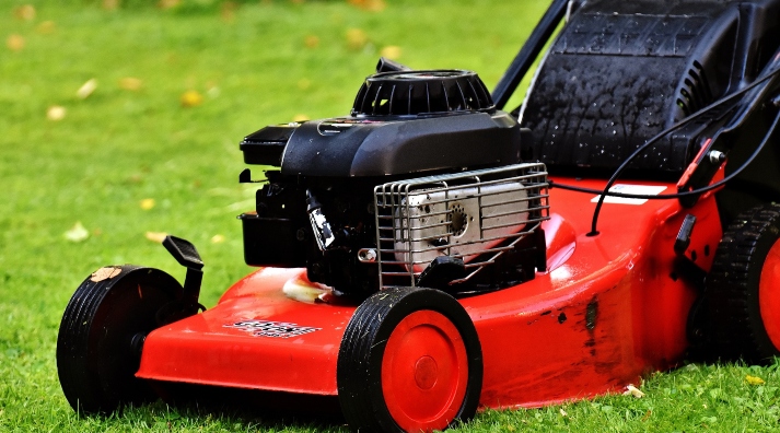 red lawn mower on healthy green grass - when is the best time of day to mow the lawn
